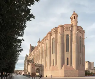 Tall rounded brick buttresses and narrow Gothic windows rise above a paved street beside Albi Cathedral.