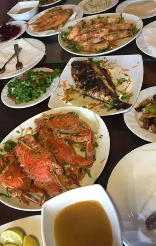 Plates of fish, prawns and crabs share a restaurant table with soup and side dishes.