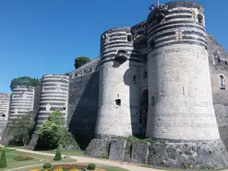 Round stone fortress towers with contrasting horizontal masonry bands above a neatly planted garden in the former moat.