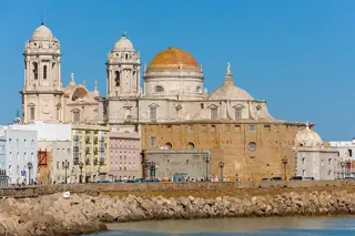A golden dome and twin pale towers rise above waterfront buildings and a stone seawall.