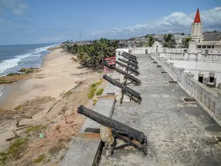 A row of dark cannons points across white ramparts toward the sea and a long sandy shoreline.