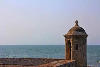 A small domed stone sentry turret on a brick-edged rampart with blue sea behind it.