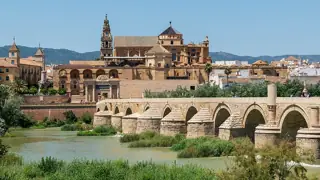 Arches of a stone bridge cross the river beneath the Mosque-Cathedral and the historic city skyline.