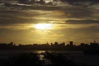Sunlight breaks through layered clouds above water and the dark silhouetted Dakar skyline.