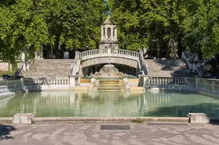 A broad pool below a carved cascade and twin stone stairways, with the Darcy monument framed by mature trees.