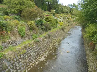A shallow stream flows between stone banks and densely planted green slopes.