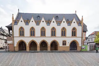 A pale town hall with pointed roof gables and arched ground-floor openings across an open cobbled square.