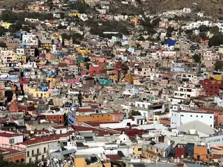 Brightly painted houses spread across a dry hillside above closely packed rooftops and streets.
