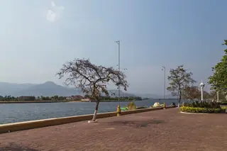 Trees and a brick promenade follow the river, with a low balustrade and distant hills across the water.