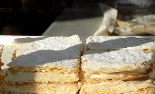 Supporting illustration photographed in Kotor: layered custard pastries behind glass in hard sunlight.