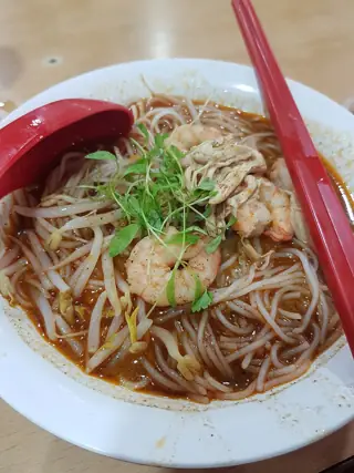 Noodles, prawns and shredded toppings in a bowl of reddish broth.
