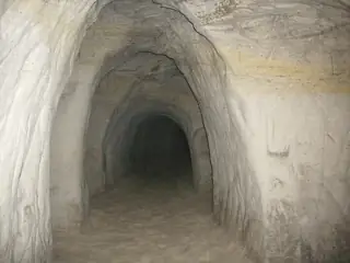 A sandy passage curves into darkness between pale layered walls, with footprints on the floor.