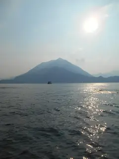 Hazy mountains and sunlight reflected on Lake Como with a small ferry.