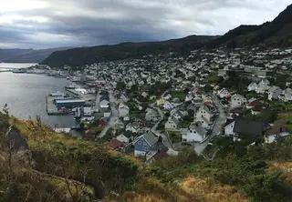 Hillside view over Måløy’s white wooden houses, waterfront quays and mountain backdrop.