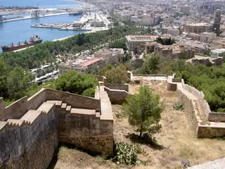 Fortress walls step down a wooded hillside toward city buildings, a green park and the blue harbour.