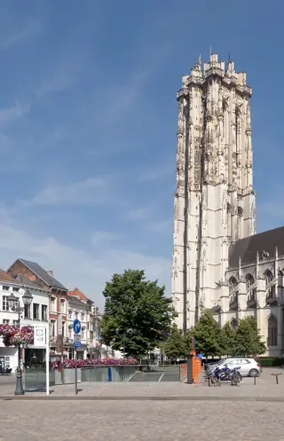 The pale stone Gothic tower rises beside the cathedral, with trees, parked vehicles and street signs below.