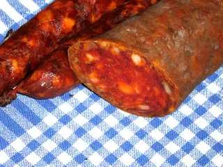 Regional food illustration of sliced Petrovački kulen on blue-and-white checked cloth; exact capture locality unspecified.