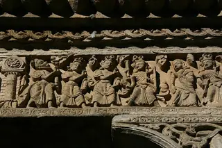 A tightly framed stone narrative relief with small figures, an animal and a tree, surrounded by weathered carved architectural bands.
