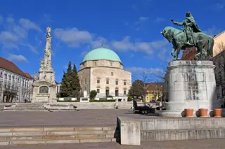 Broad paved square below a domed stone building, with a tall Trinity monument and an equestrian statue.