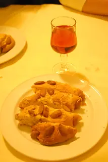 Food illustration photographed in Pistoia in 2010: cantucci on a plain white plate beside a glass of wine.