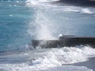 White spray rises over a low dark sea barrier amid turquoise waves.