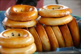 Golden round breads stacked upright and in pairs on a blue-green cloth, with shallow-focus foreground loaves.