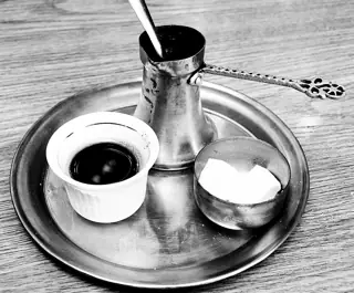 Black-and-white view of coffee in a small cup beside a metal pot and sugar.