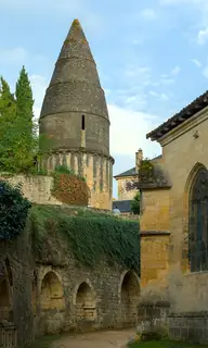 Round stone tower with a tall conical roof above ivy-covered walls and arched burial recesses, with part of a stone church at right.