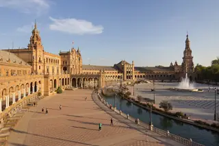 Broad semicircular plaza, canal and fountain surrounded by arcaded buildings.