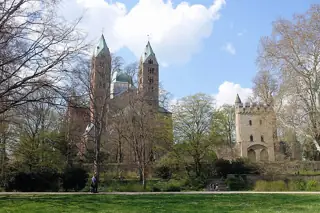 Cathedral towers and a smaller stone tower rise behind trees, lawn and a garden stairway.