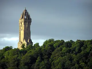 Stone tower rising above green trees beneath a blue and gray clouded sky.