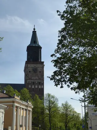 Supporting illustration photographed in Turku, Finland: tall cathedral tower and spire rising above a tree-lined street and neighboring classical façades.