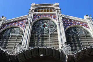 Ornate market masonry, patterned glazing and ironwork beneath a blue sky.