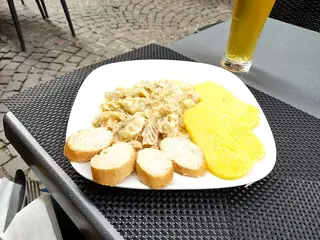 A white plate holds a serving of fish, yellow polenta and sliced bread on a woven table mat.