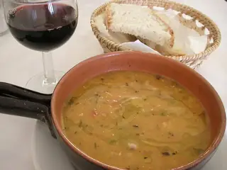Regional food illustration of acquacotta soup in a plain pan beside bread and wine; capture locality unspecified.