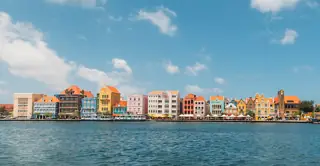 Colorful gabled buildings line the far waterfront above blue water beneath a broad cloudy sky.