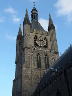 Upward view of the stone belfry, its gold clock and pointed corner turrets against blue sky.
