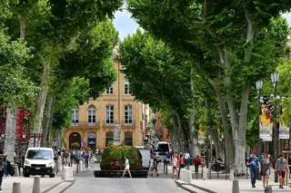 A tree-lined avenue with pale stone buildings, a fountain and pedestrians.