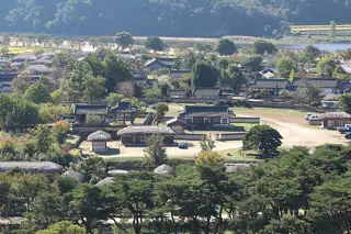 Tiled and thatched roofs cluster among trees, low walls and open courtyards.
