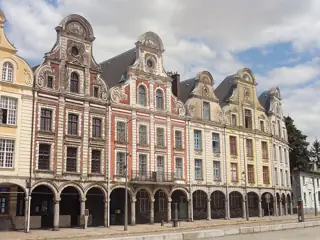 Red-brick and pale-stone gabled houses stand above a continuous row of shaded arcades.