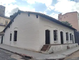 White corner house with a tiled roof, barred windows and brick steps beside the pavement.