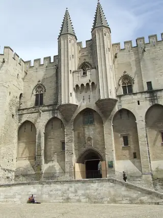 Tall pointed stone towers above Gothic windows and the arched palace entrance, with battlements and two small figures at ground level.
