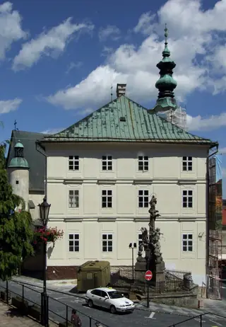A pale three-story town hall with a green roof and slender spire faces a small paved square.