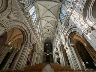 Rows of wooden chairs beneath carved stone arcades and a high ribbed vault inside Bayeux Cathedral.