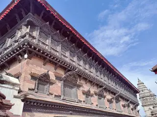 A long red-brick palace facade has rows of intricately carved dark wooden windows beneath a deep tiled roof.