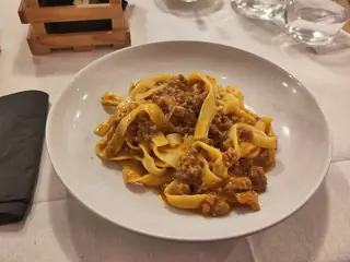 Golden ribbon pasta coated in meat ragù on a white plate at a restaurant table.