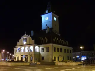 The pale Council House and its lit clock tower stand beside an empty paved square beneath a dark night sky.
