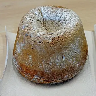 A tall golden ring-shaped bossolà cake dusted with powdered sugar on a paper-covered table.