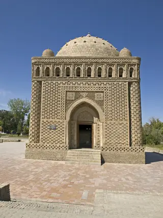 A compact domed brick mausoleum has an arched entrance, patterned walls and a row of small arches below the roof.