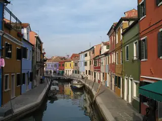 A narrow canal reflects rows of colourful houses, with boats tied beside the paved banks.